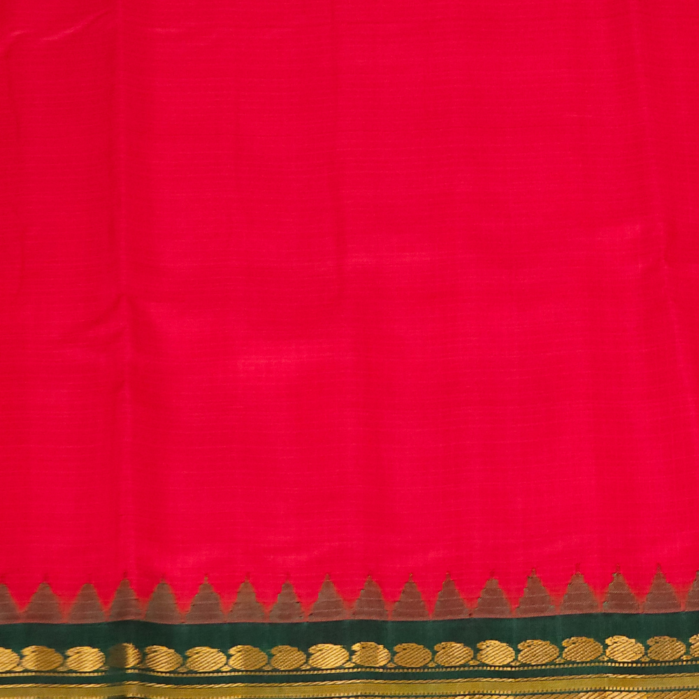 A vibrant red silk saree with a detailed gold and green zari border, featuring a small peacock logo in the top right corner.