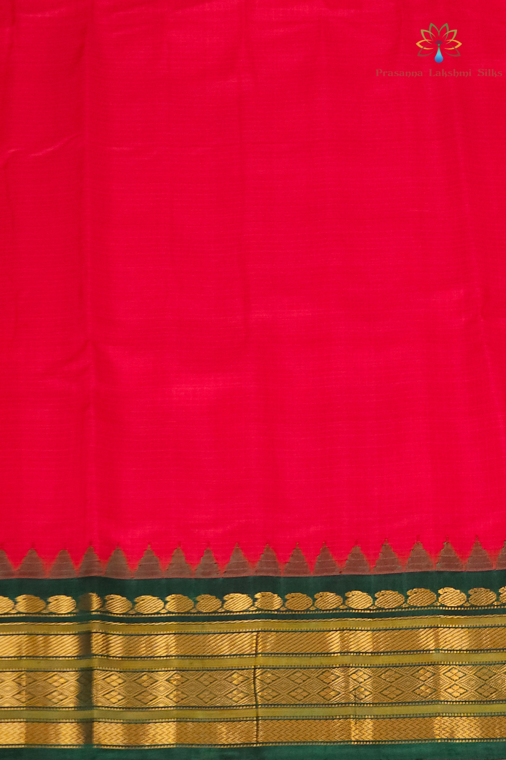 A vibrant red silk saree with a detailed gold and green zari border, featuring a small peacock logo in the top right corner.