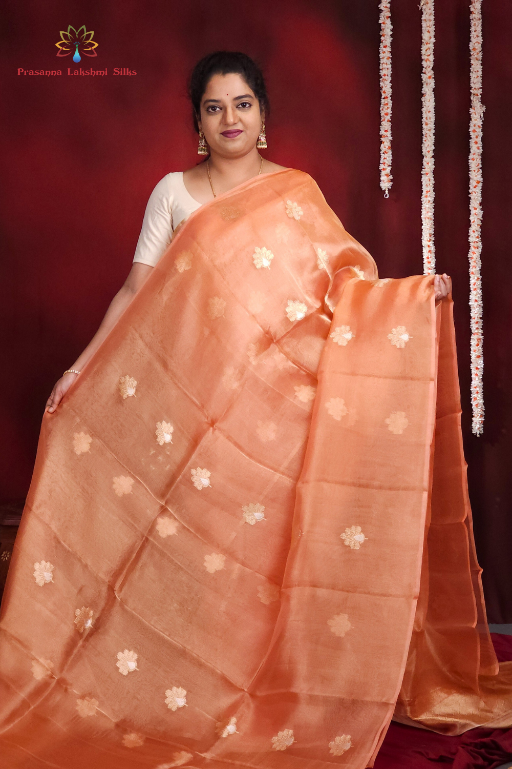 Woman wearing a peach saree with white floral patterns against a red background