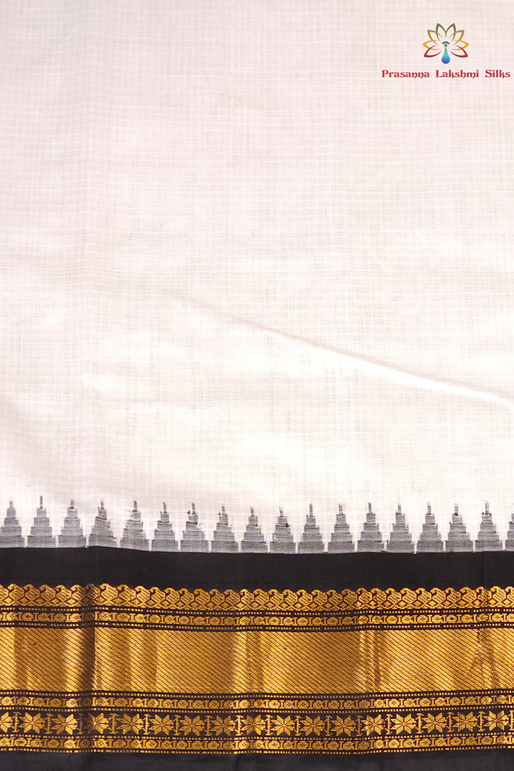 A close-up of a white or off-white fabric saree body with a black border and ornate gold zari embroidery, featuring a repeating small motif along the edge. A logo for 'Princess Lakshmi Silks' is visible in the top right corner.