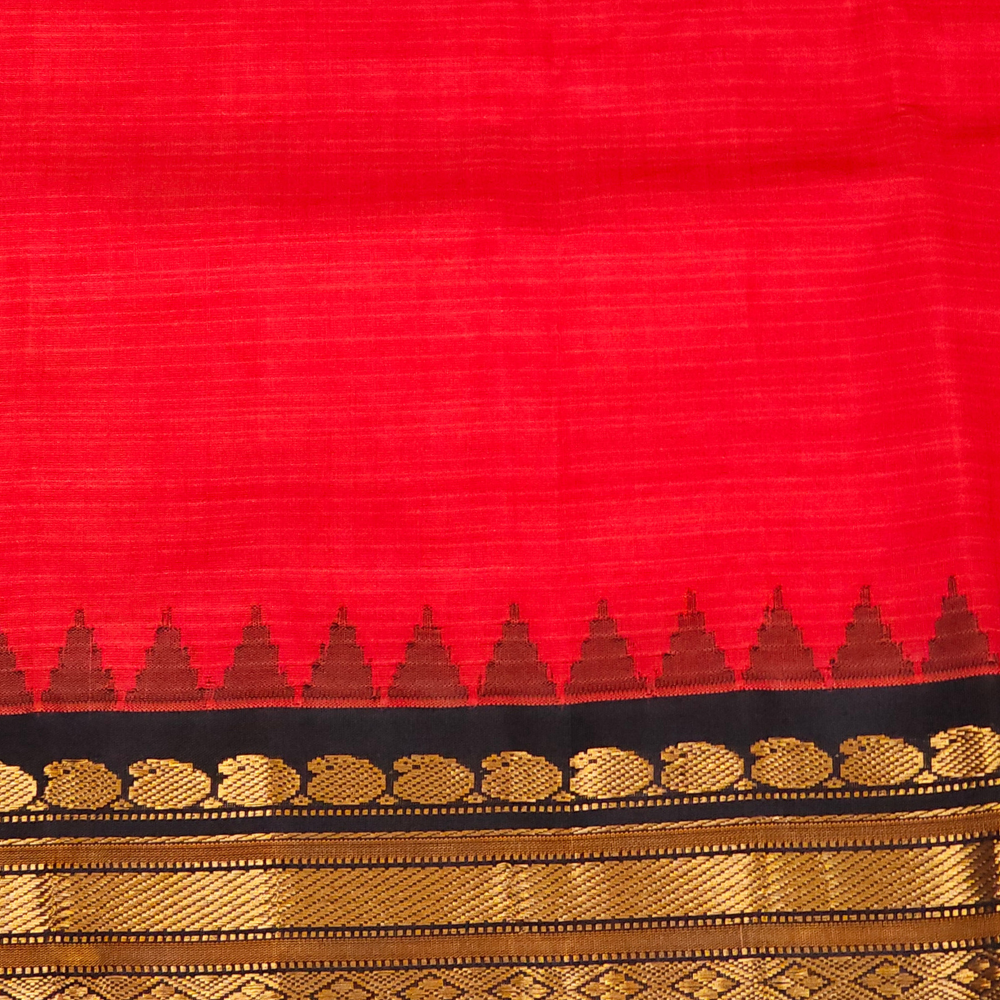 A close-up of a red fabric, likely a saree, featuring a black border with metallic gold zari woven patterns and a row of small gold triangles.